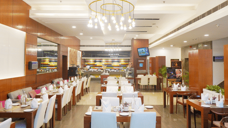 A wide angle view of the  restaurant interior at Nemesia featuring chandeliers, wooden furniture, tables arranged with napkins, water glasses, and plates