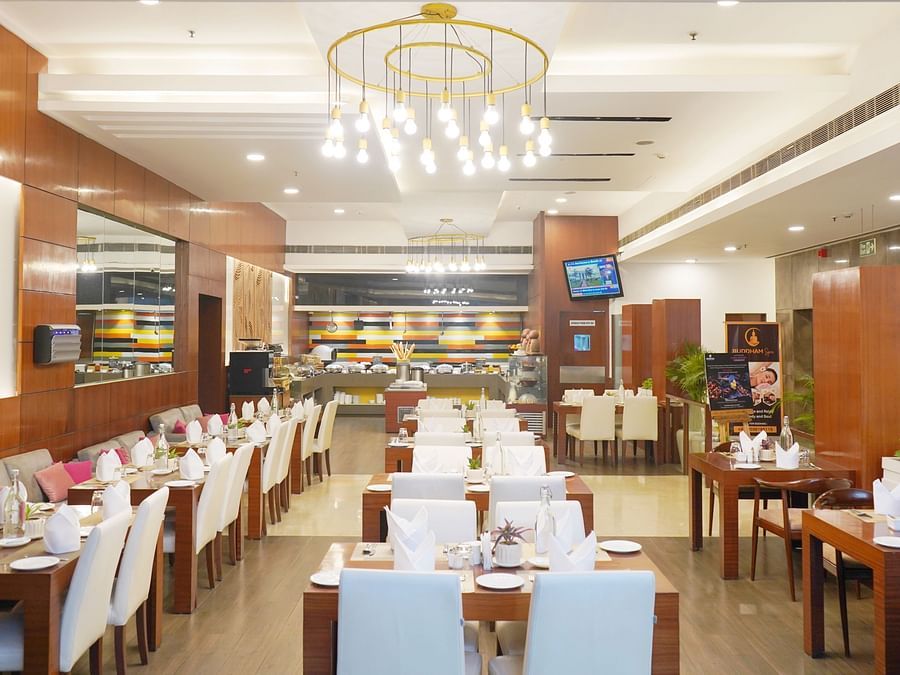 A wide angle view of the  restaurant interior at Nemesia featuring chandeliers, wooden furniture, tables arranged with napkins, water glasses, and plates