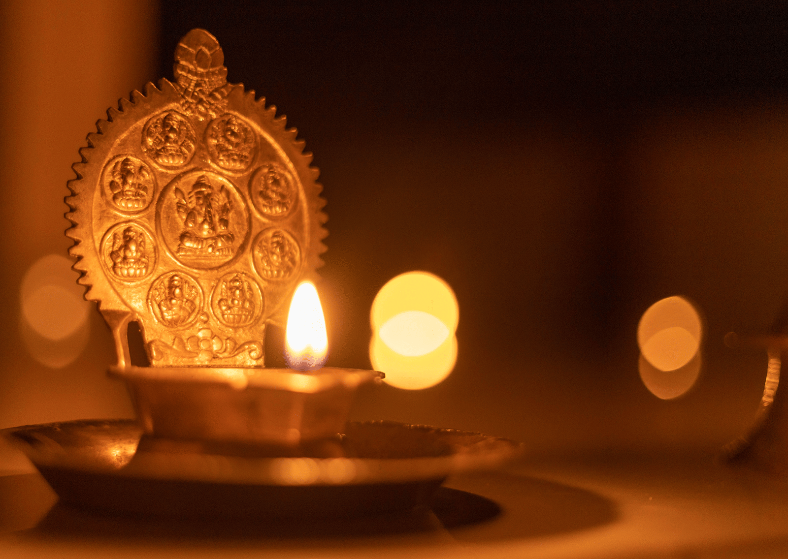 An ornate glowing brass diya oil lamp illuminated in a dark setting.