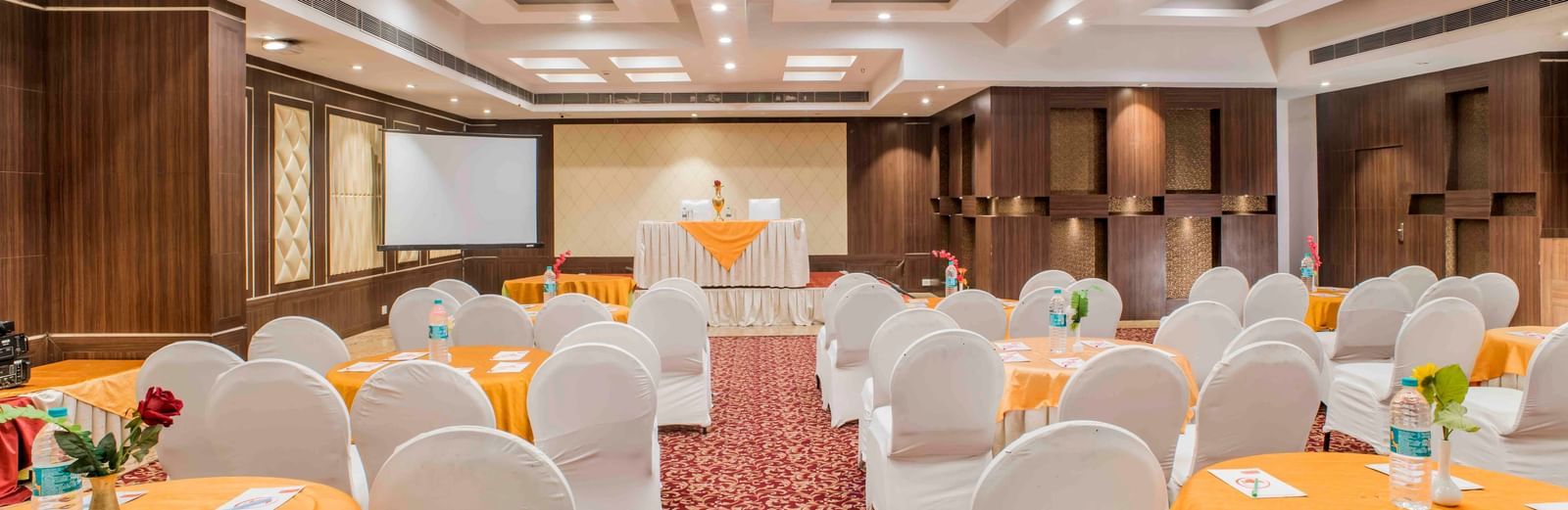 A large banquet hall with round tables and chairs ready for a function at The Citi Residenci Hotel, Durgapur.