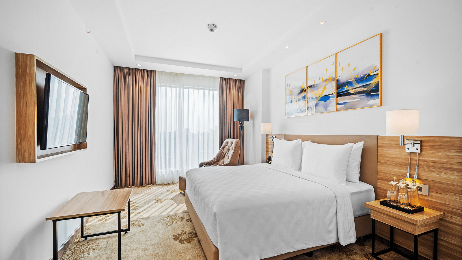 An image of a king size bed in front of a TV of a Deluxe Room at Grand Vijayawada by GRT Hotels.