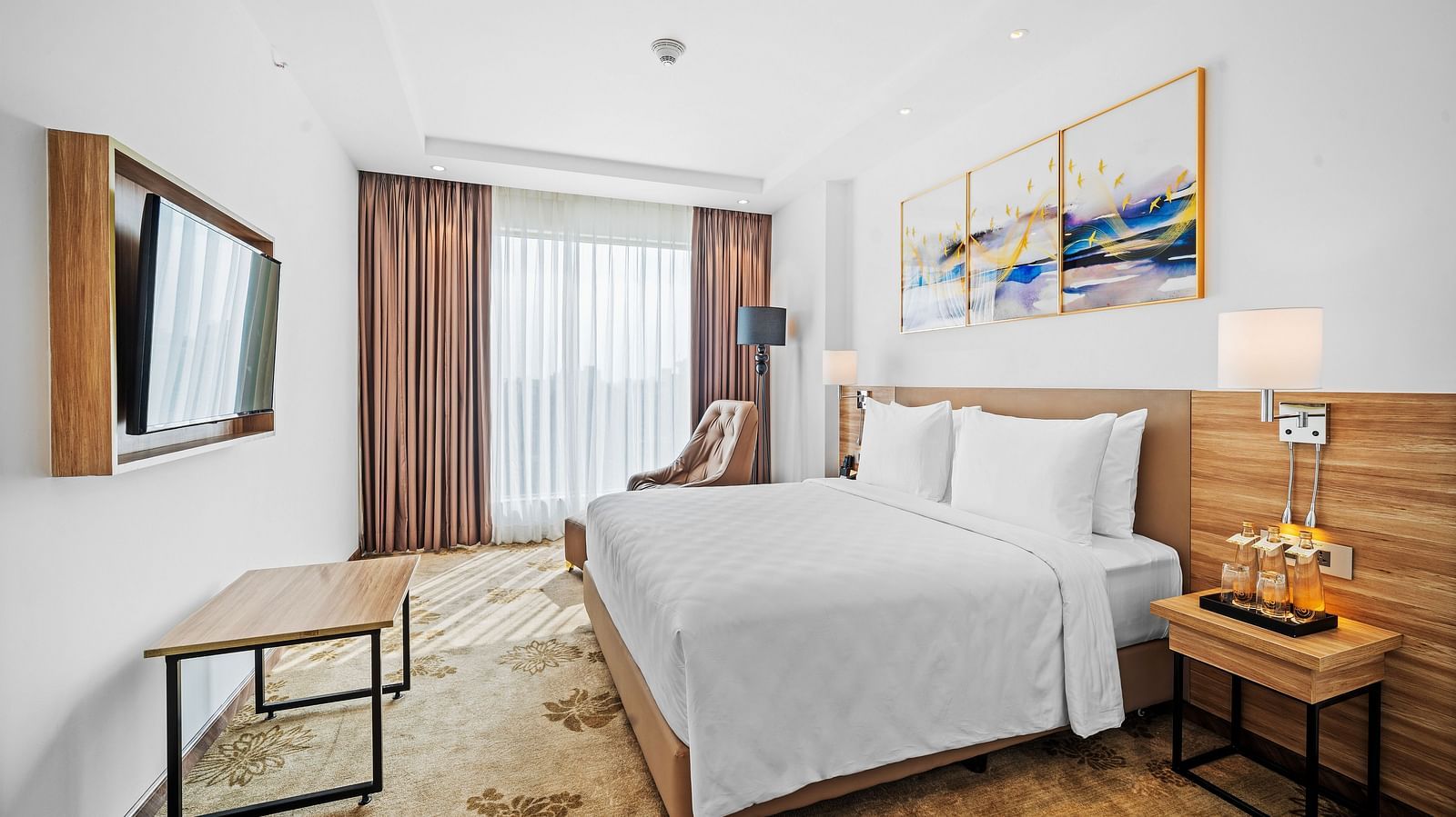An image of a king size bed in front of a TV of a Deluxe Room at Grand Vijayawada by GRT Hotels.