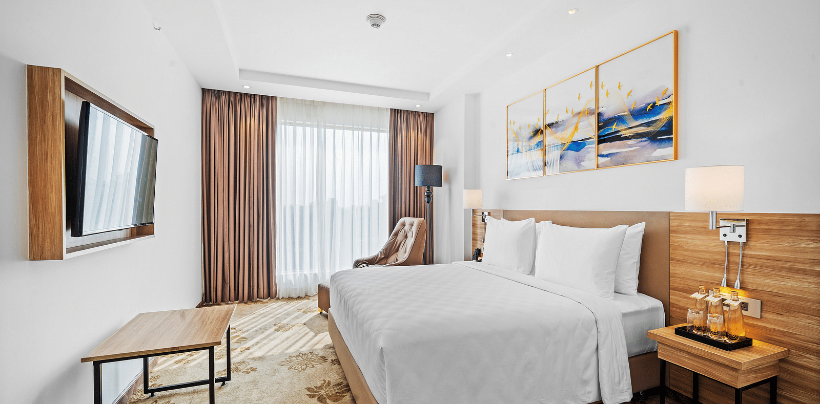 An image of a king size bed in front of a TV of a Deluxe Room at Grand Vijayawada by GRT Hotels.