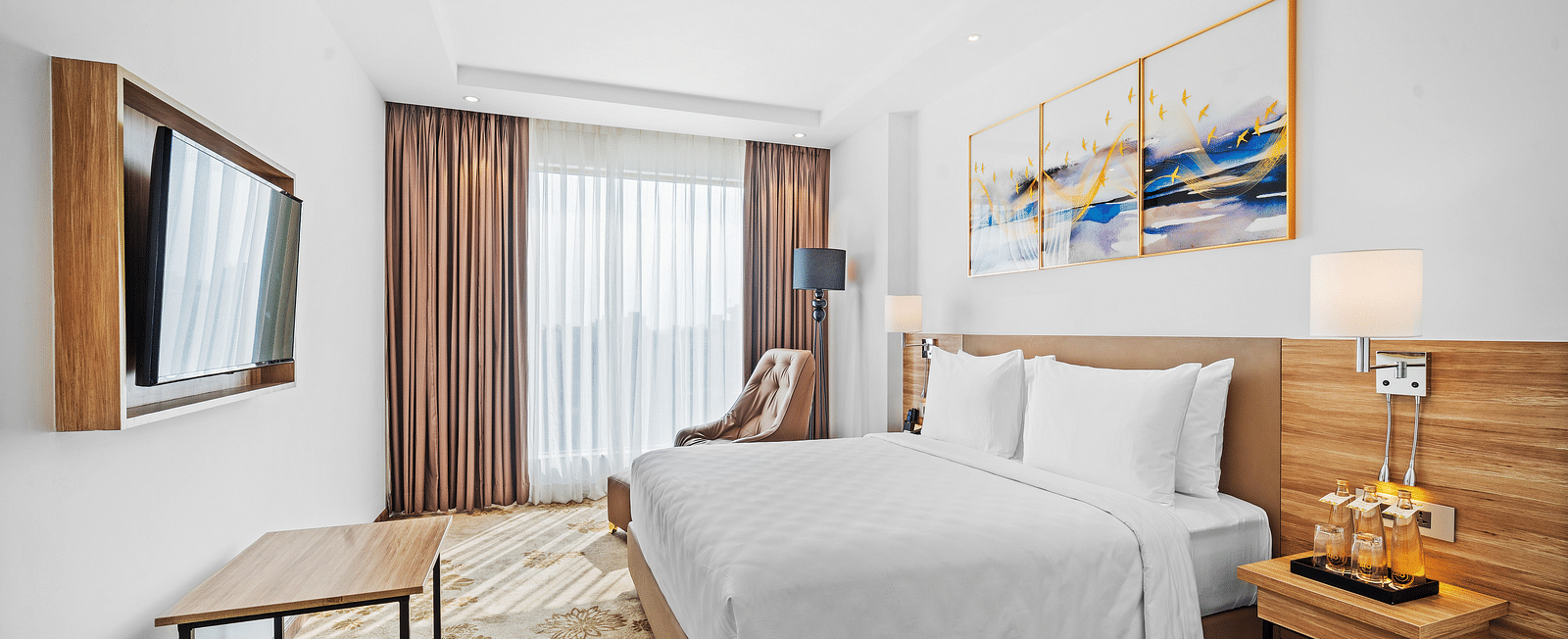 An image of a king size bed in front of a TV of a Deluxe Room at Grand Vijayawada by GRT Hotels.