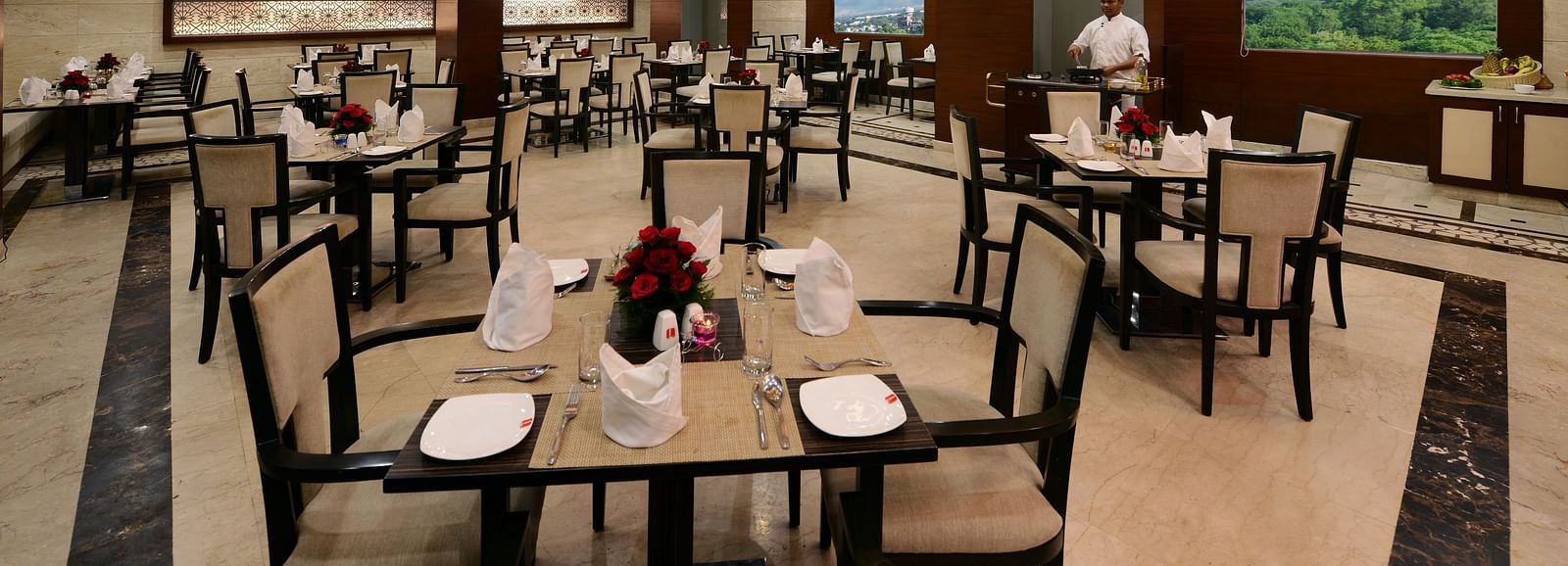 A restaurant seating area with neatly arranged chairs and tables, well-lit ambience and glass windows overlooking greenery