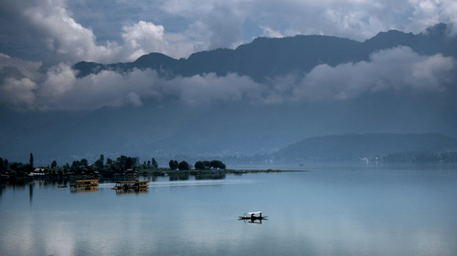 An image of a boat sailing in the Dal Lake with mountains in the background