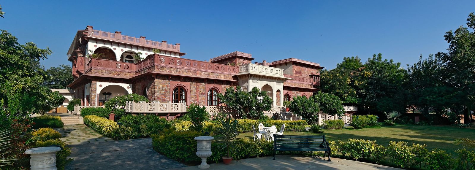 A grand Indian villa's walkway surrounded by lush gardens under a clear blue sky - Khas Bagh, Jaipur.