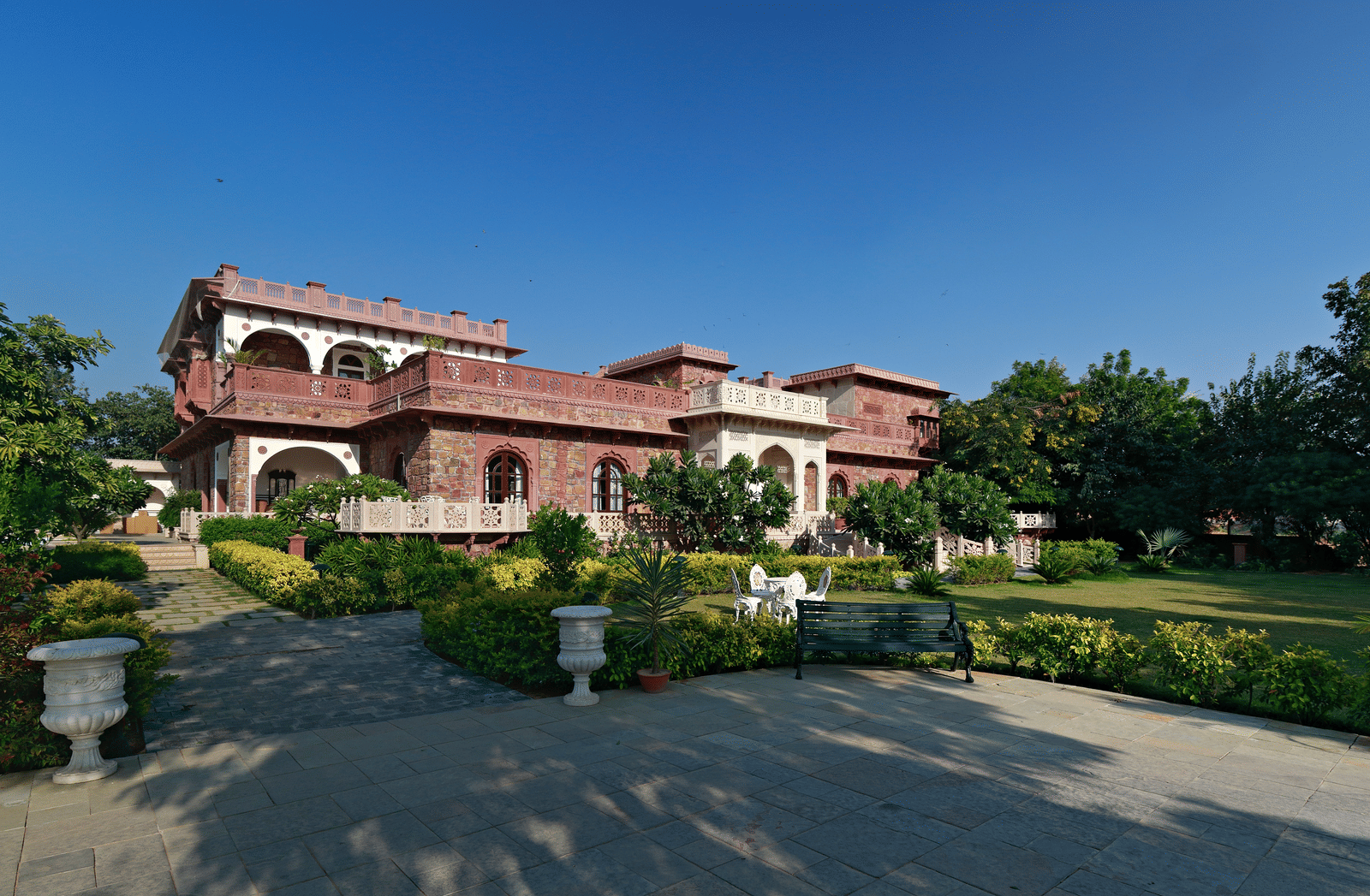 A grand Indian villa's walkway surrounded by lush gardens under a clear blue sky - Khas Bagh, Jaipur.