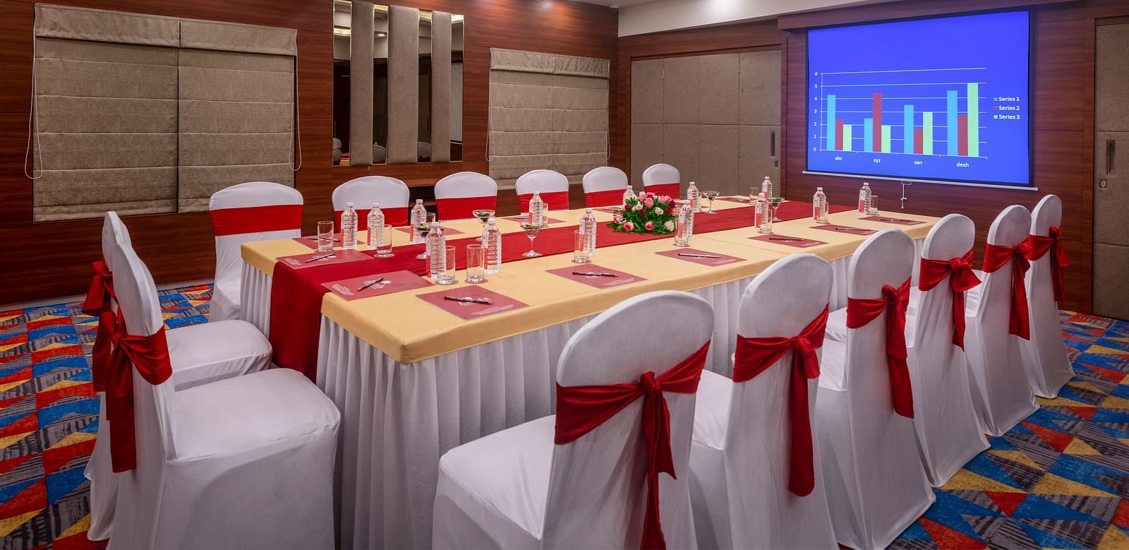 A meeting room with a long table surrounded by chairs and a projection screen displaying a presentation.
