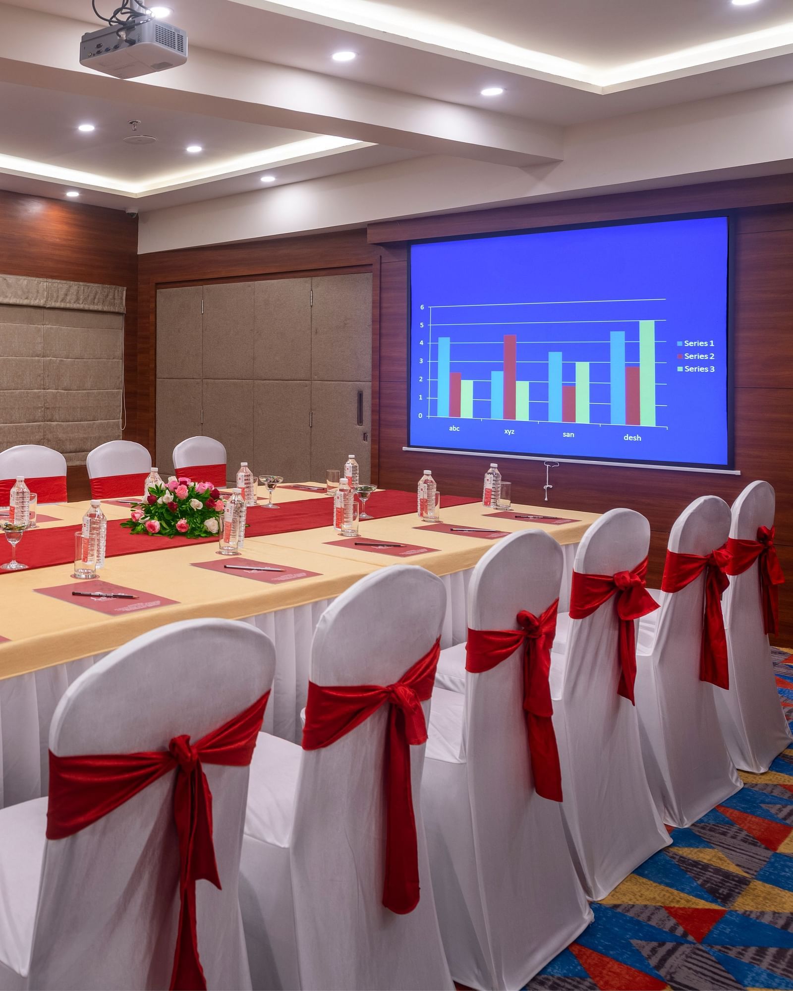 A meeting room with a long table surrounded by chairs and a projection screen displaying a presentation.