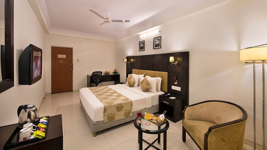 A hotel bedroom with a double bed, bedside tables, and a wicker armchair - Lords Eco Inn Dahej