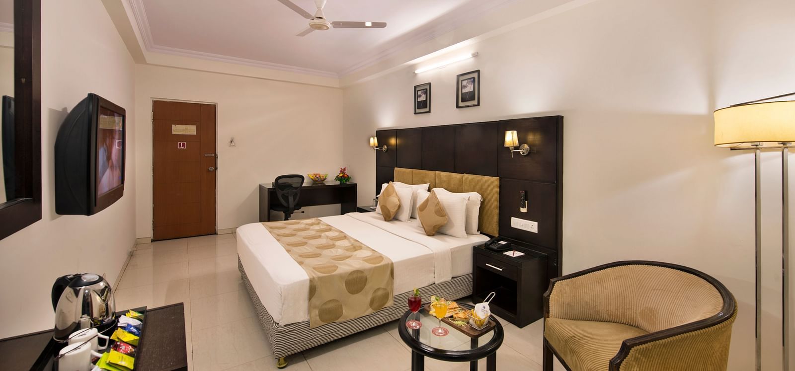 A hotel bedroom with a double bed, bedside tables, and a wicker armchair - Lords Eco Inn Dahej