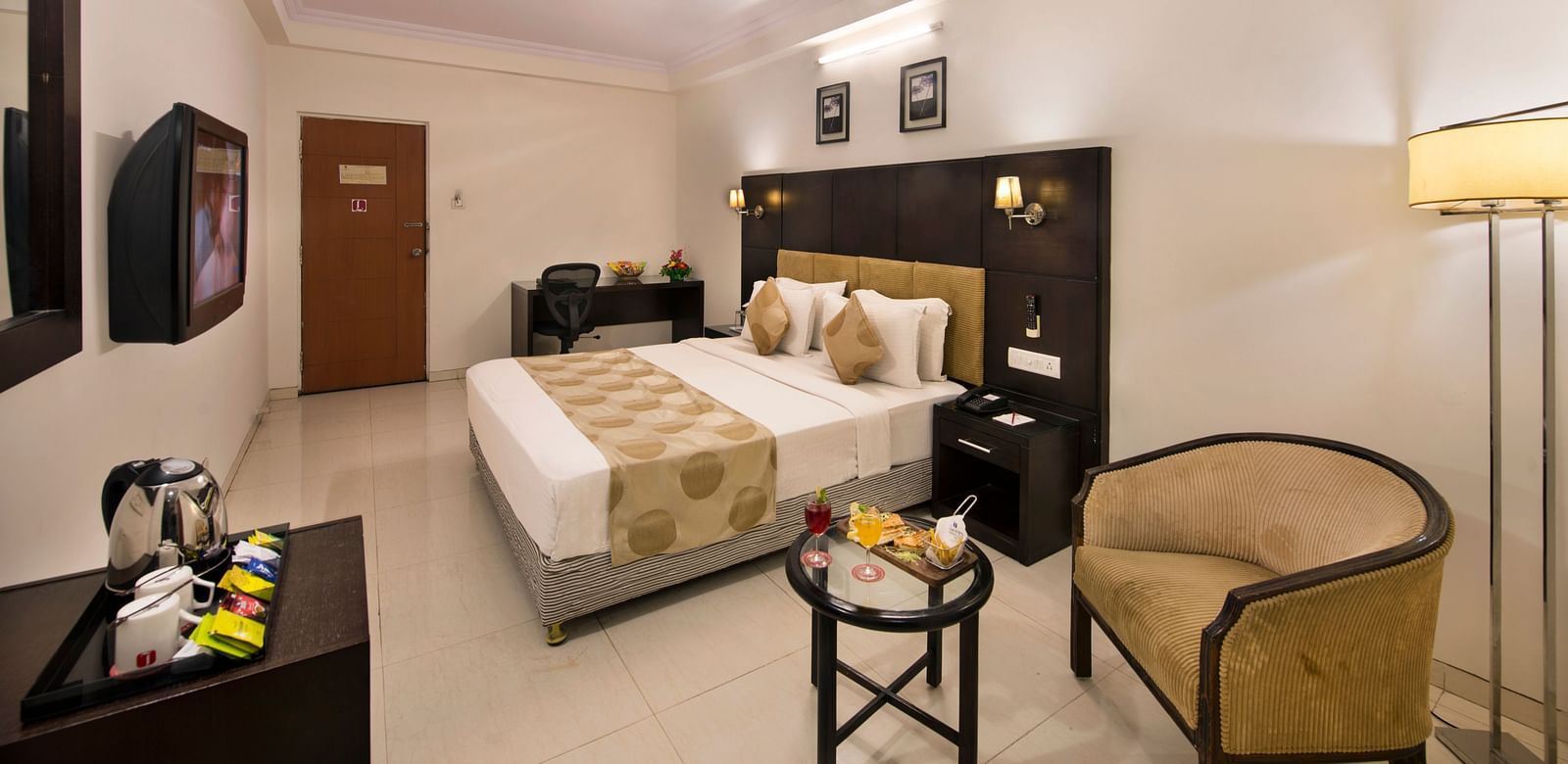 A hotel bedroom with a double bed, bedside tables, and a wicker armchair - Lords Eco Inn Dahej