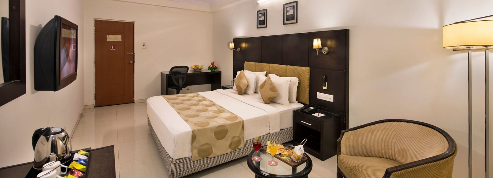 A hotel bedroom with a double bed, bedside tables, and a wicker armchair - Lords Eco Inn Dahej