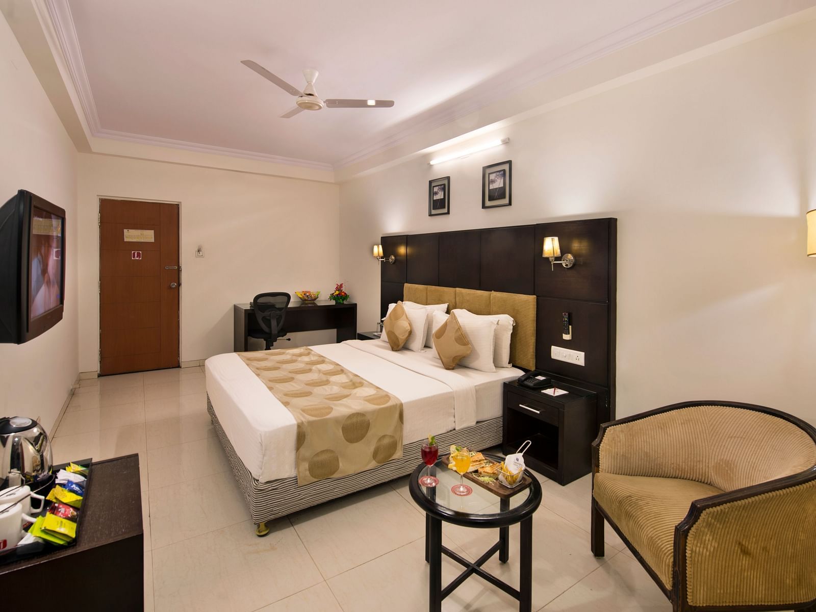 A hotel bedroom with a double bed, bedside tables, and a wicker armchair - Lords Eco Inn Dahej