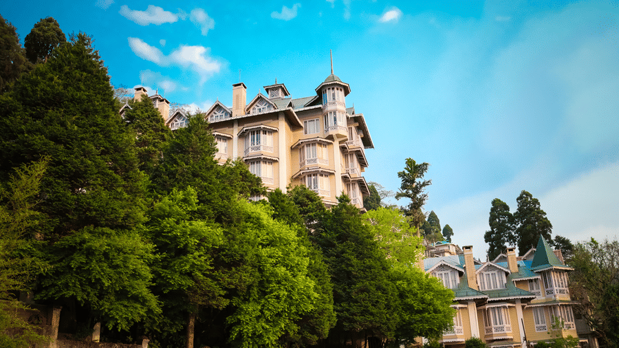 Cedar Inn, Darjeeling nestled amid lush green trees, showcasing its charming colonial architecture against a clear blue sky in the Himalayan foothills.