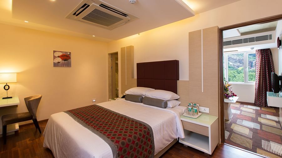 A double bed with a cushioned headboard and a side table next to it inside Suite at Hotel Pai Viceroy Tirupathi