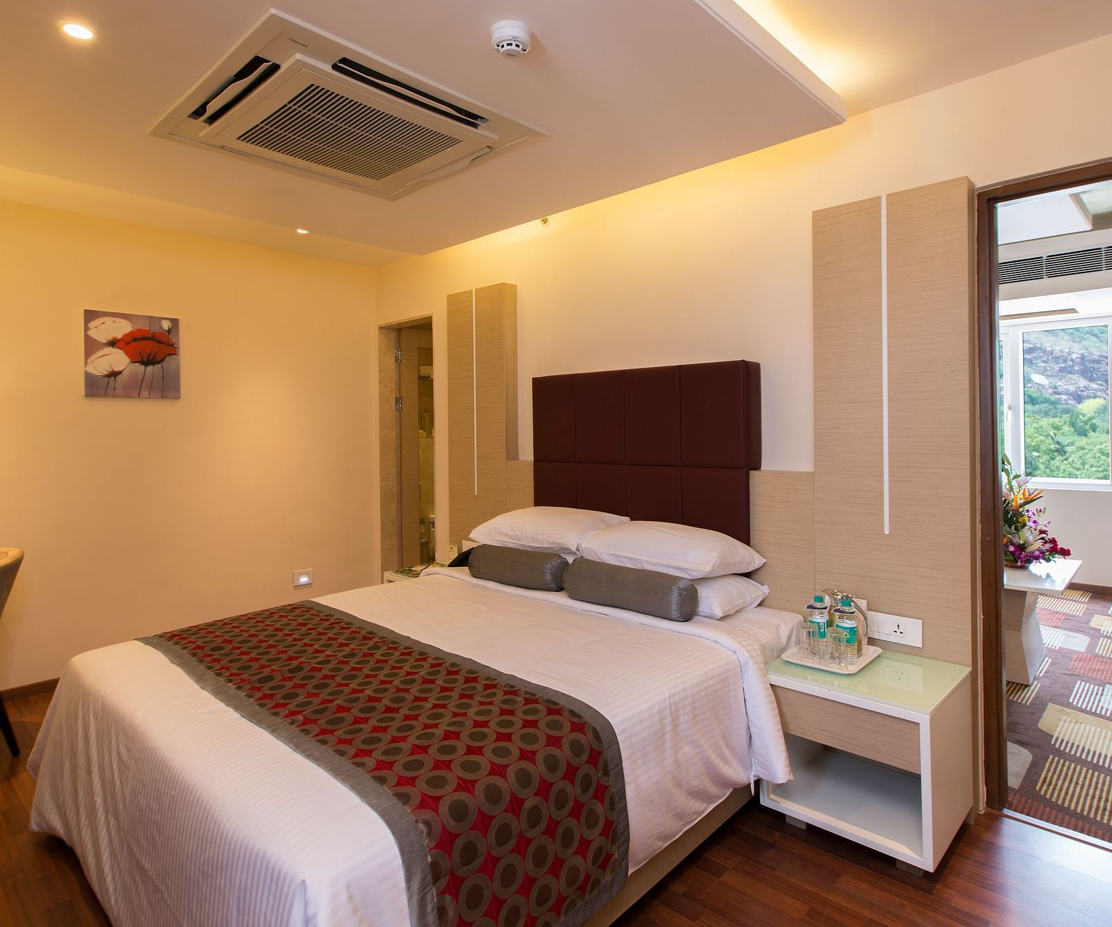 A double bed with a cushioned headboard and a side table next to it inside Suite at Hotel Pai Viceroy Tirupathi