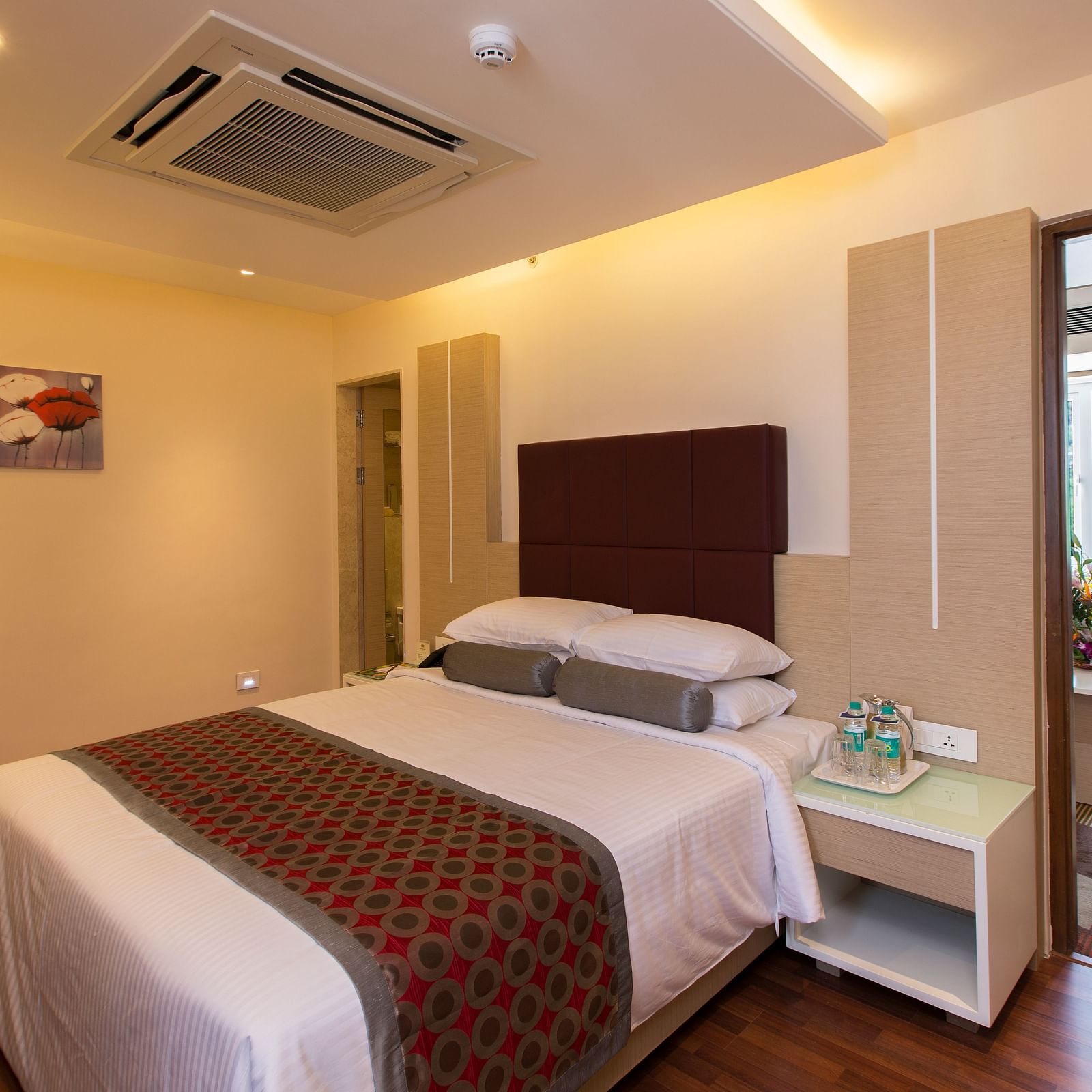 A double bed with a cushioned headboard and a side table next to it inside Suite at Hotel Pai Viceroy Tirupathi