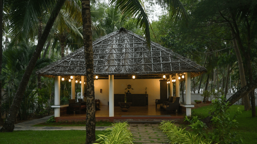 A traditional thatched-roof pavilion at Ayur On The Beach Nattika, warmly lit at dusk and surrounded by tropical palm trees.
