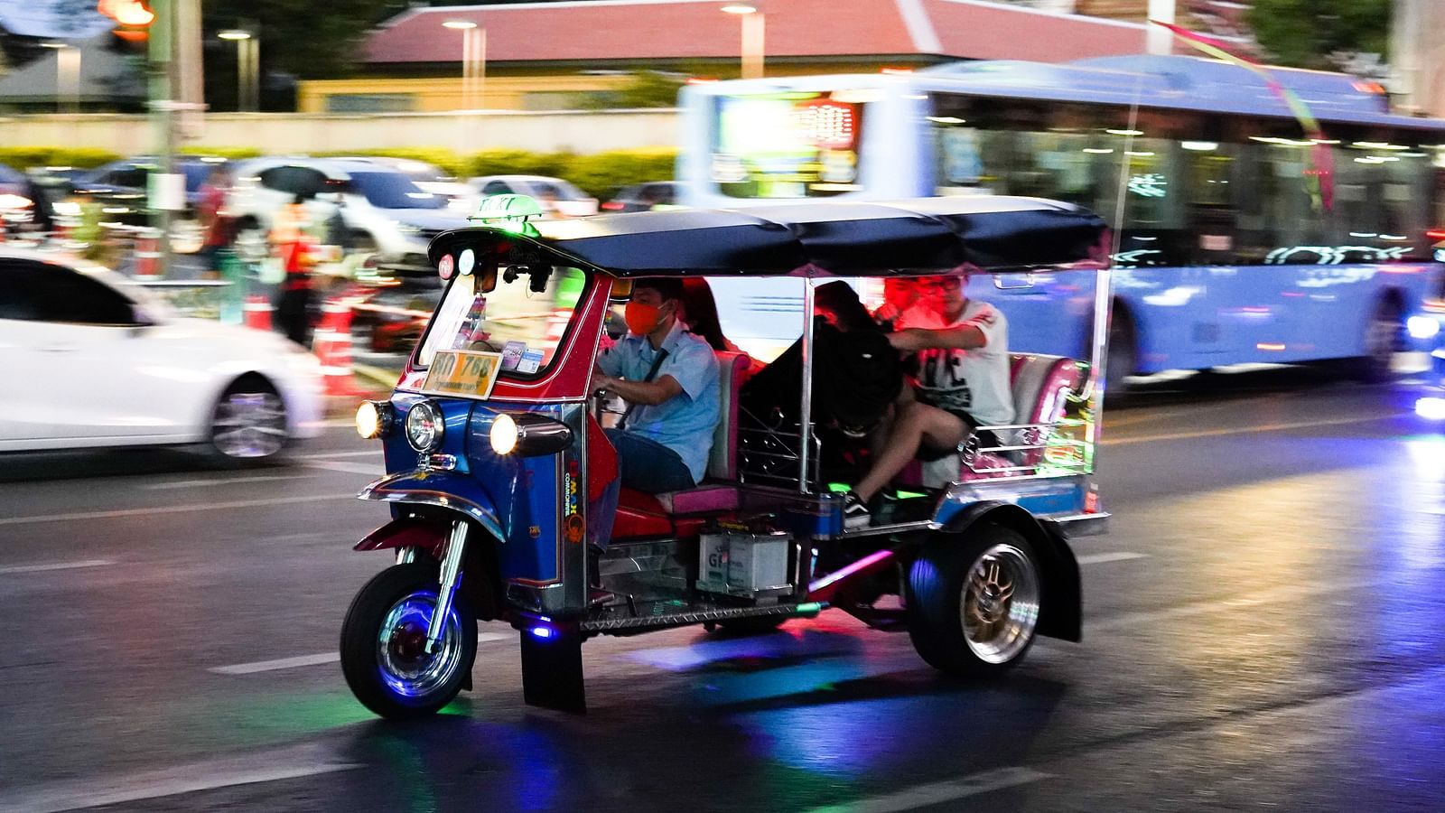 A tuk tuk travelling on a street of Bangkok with passengers inside.