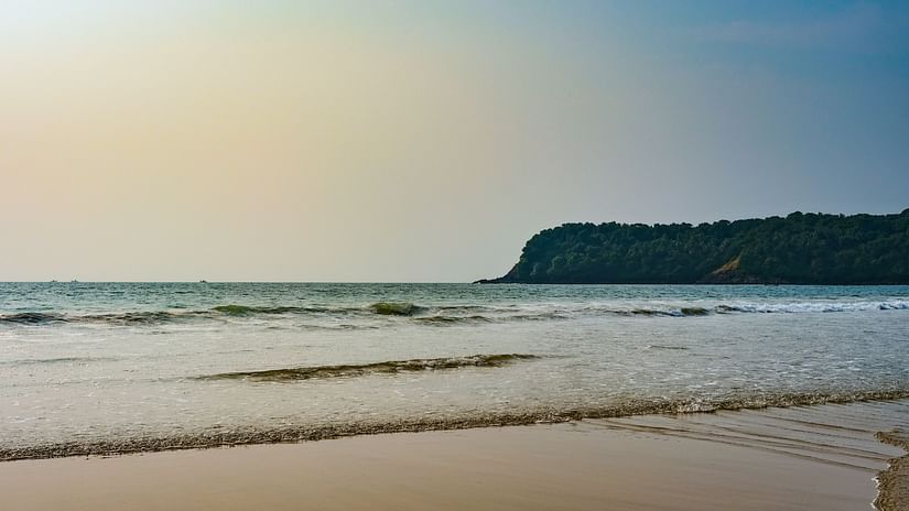 An overview of Agonda Beach with a hill in the distance and waves overlapping on the beach.