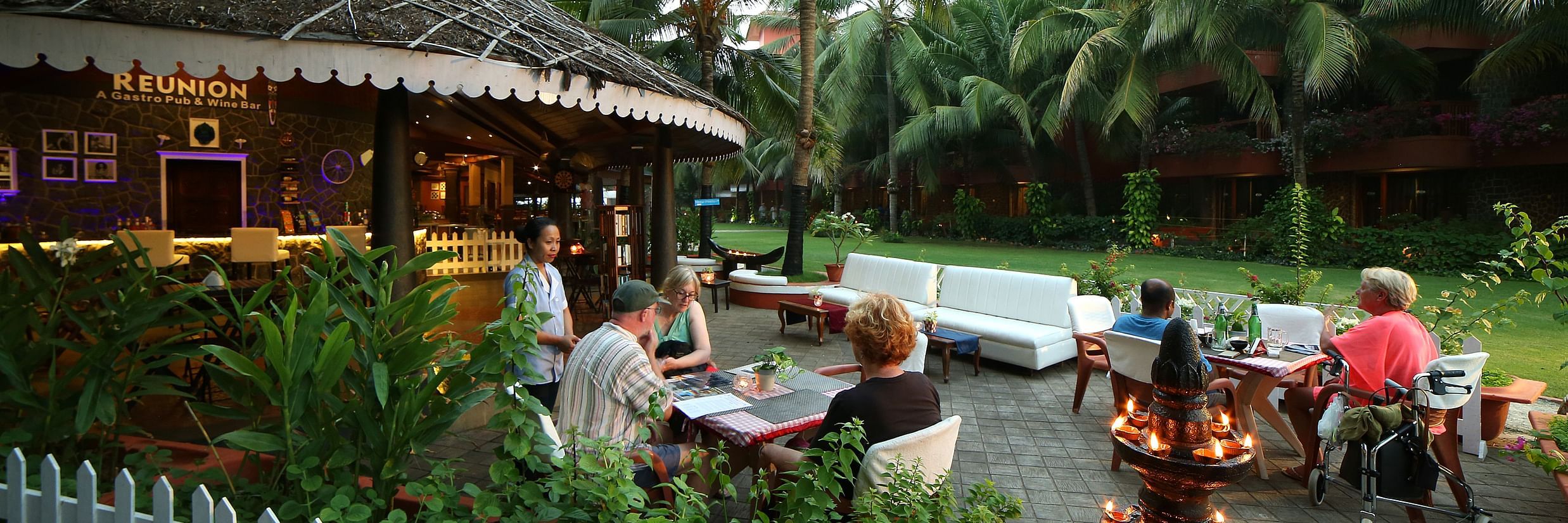 Guests dining outdoors at Uday Samudra Leisure Beach Hotel, enjoying the tropical ambience with palm trees and warm lighting