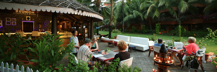 Guests dining outdoors at Uday Samudra Leisure Beach Hotel, enjoying the tropical ambience with palm trees and warm lighting
