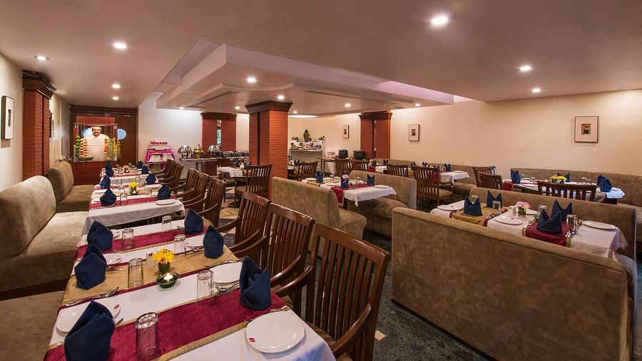 A warmly lit hotel restaurant shows multiple set tables ready for diners - Lords Inn Vadodara 