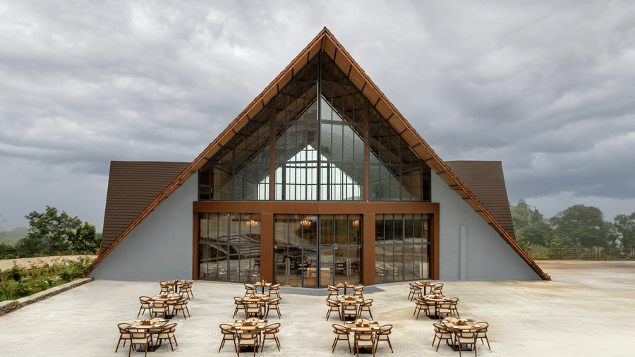 The entrance to a large A-frame building with an outdoor seating area and dining tables set up on a paved patio at the Osian Valley Resort & Spa.