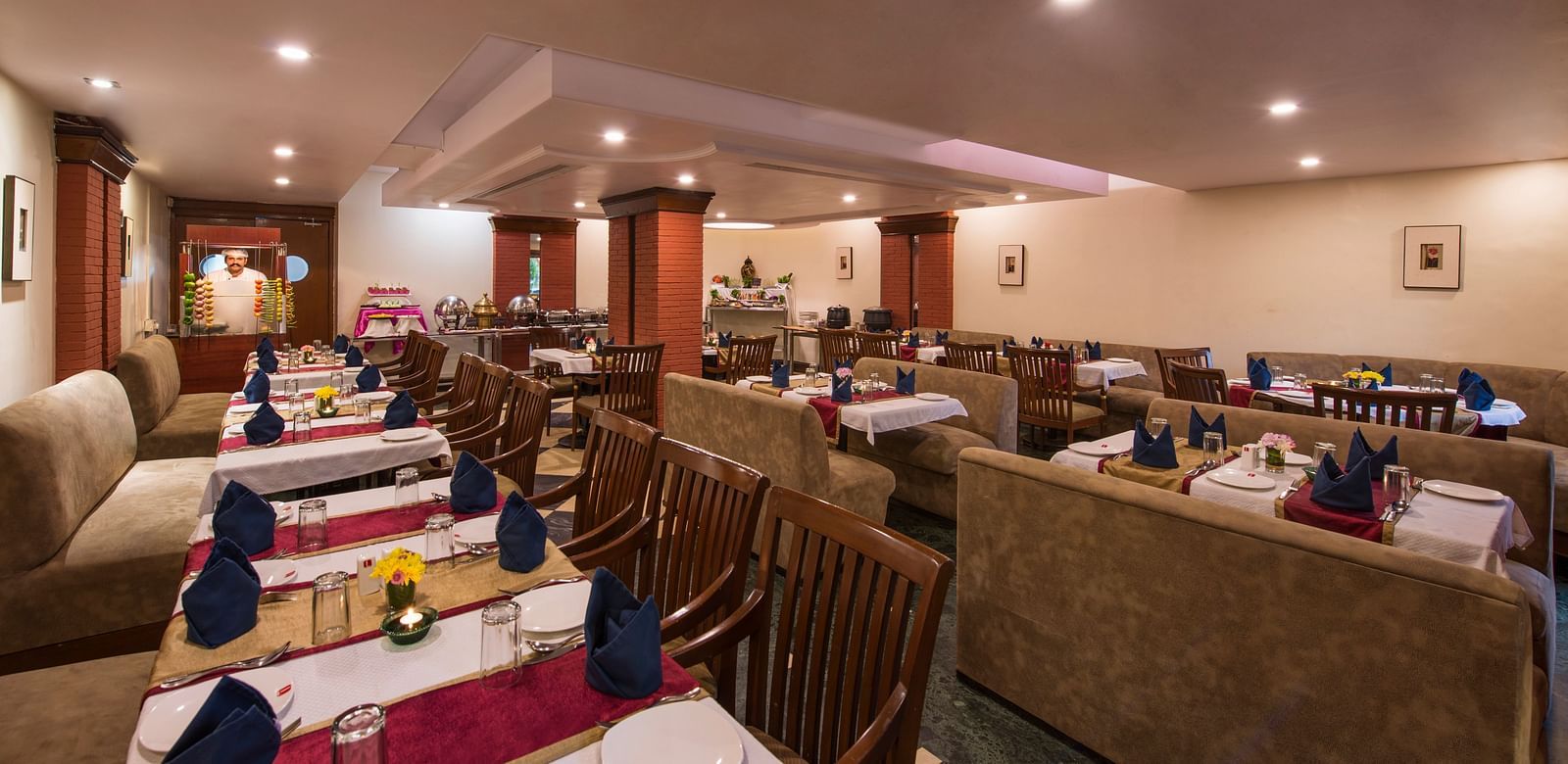 A warmly lit hotel restaurant shows multiple set tables ready for diners - Lords Inn Vadodara 