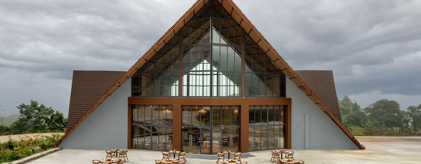 The entrance to a large A-frame building with an outdoor seating area and dining tables set up on a paved patio at the Osian Valley Resort & Spa.