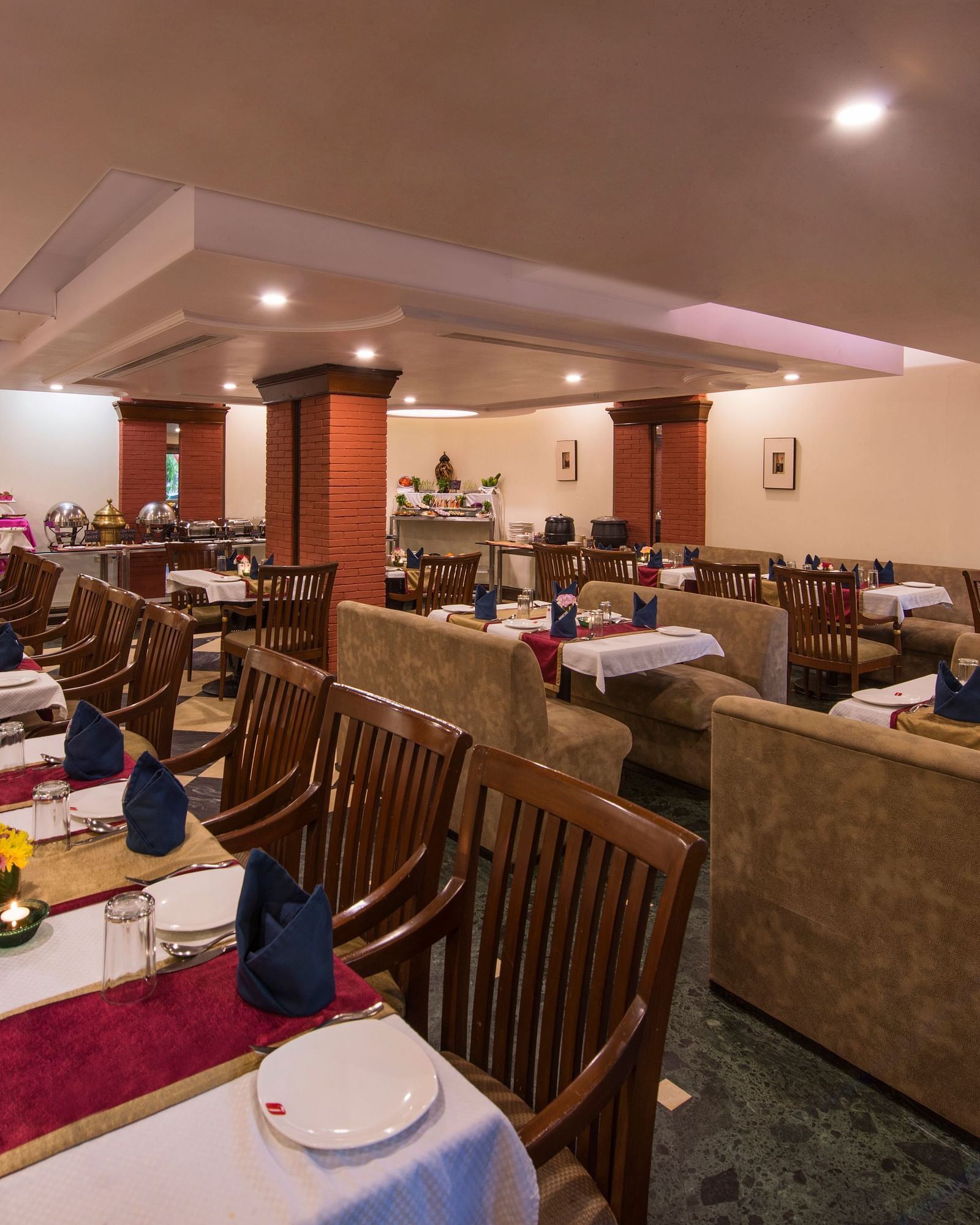 A warmly lit hotel restaurant shows multiple set tables ready for diners - Lords Inn Vadodara 