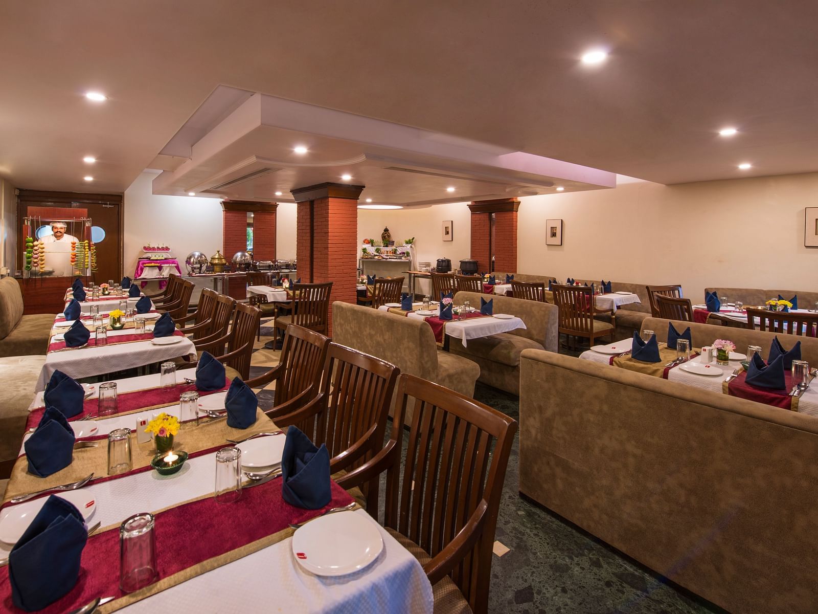 A warmly lit hotel restaurant shows multiple set tables ready for diners - Lords Inn Vadodara 