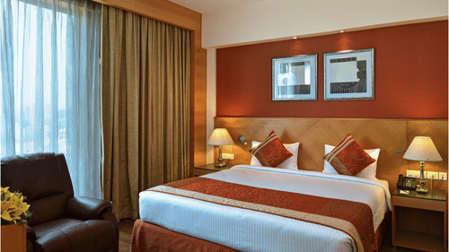 Modern room at Savoy Suites, Noida featuring contemporary design, leather recliner, floor-to-ceiling windows, and stylish furnishings