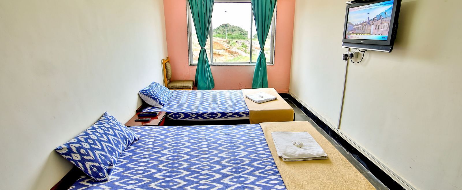A side view of three beds with bedding in a room with a window and TV at Hotel Sahara - Comfortable Accommodations in Ramoji Film City, Hyderabad.