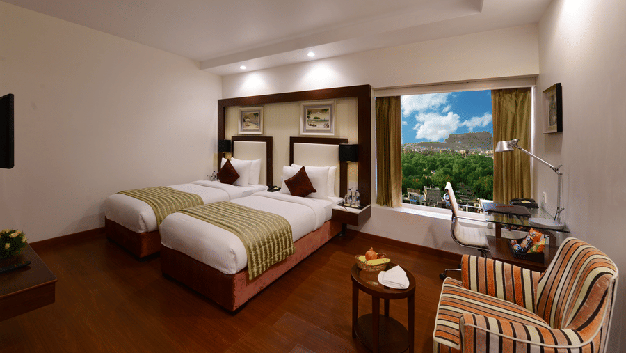 Twin bed room with a glass window with greenery view, a sofa and work desk