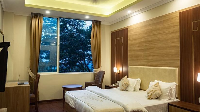 A queen bed with a large window next to it inside Deluxe Room at Sumitel Gangtok