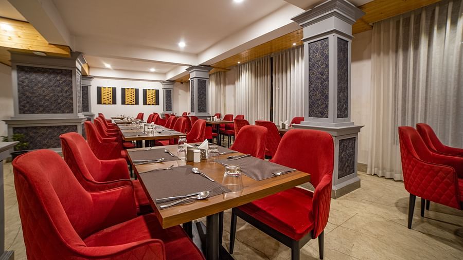 Dining area in Sumitel Hotel with multiple red-cushioned chairs and tables, stylish lighting, and patterned wall panels.