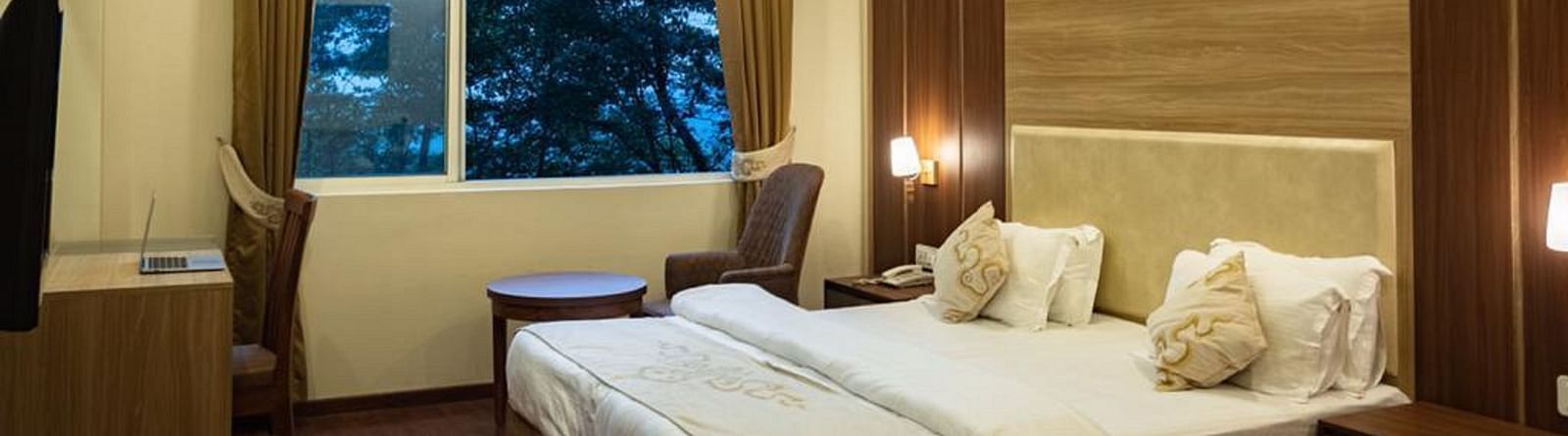 A queen bed with a large window next to it inside Deluxe Room at Sumitel Gangtok 