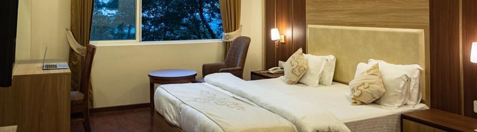 A queen bed with a large window next to it inside Deluxe Room at Sumitel Gangtok 