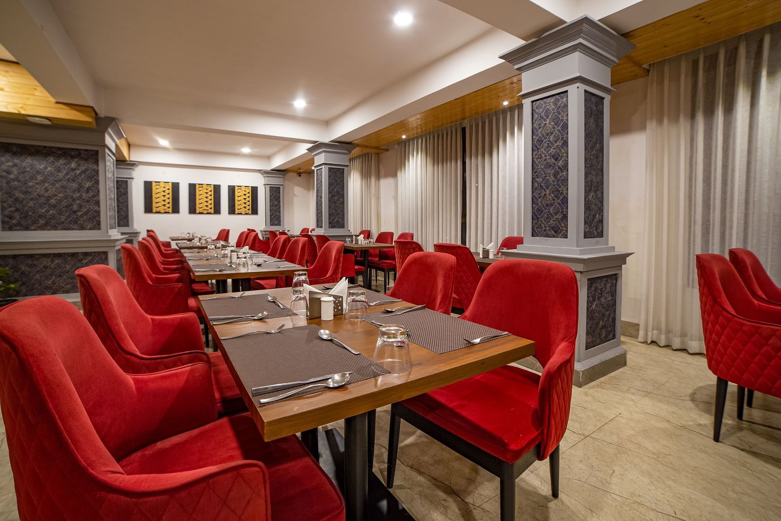 Dining area in Sumitel Hotel with multiple red-cushioned chairs and tables, stylish lighting, and patterned wall panels.