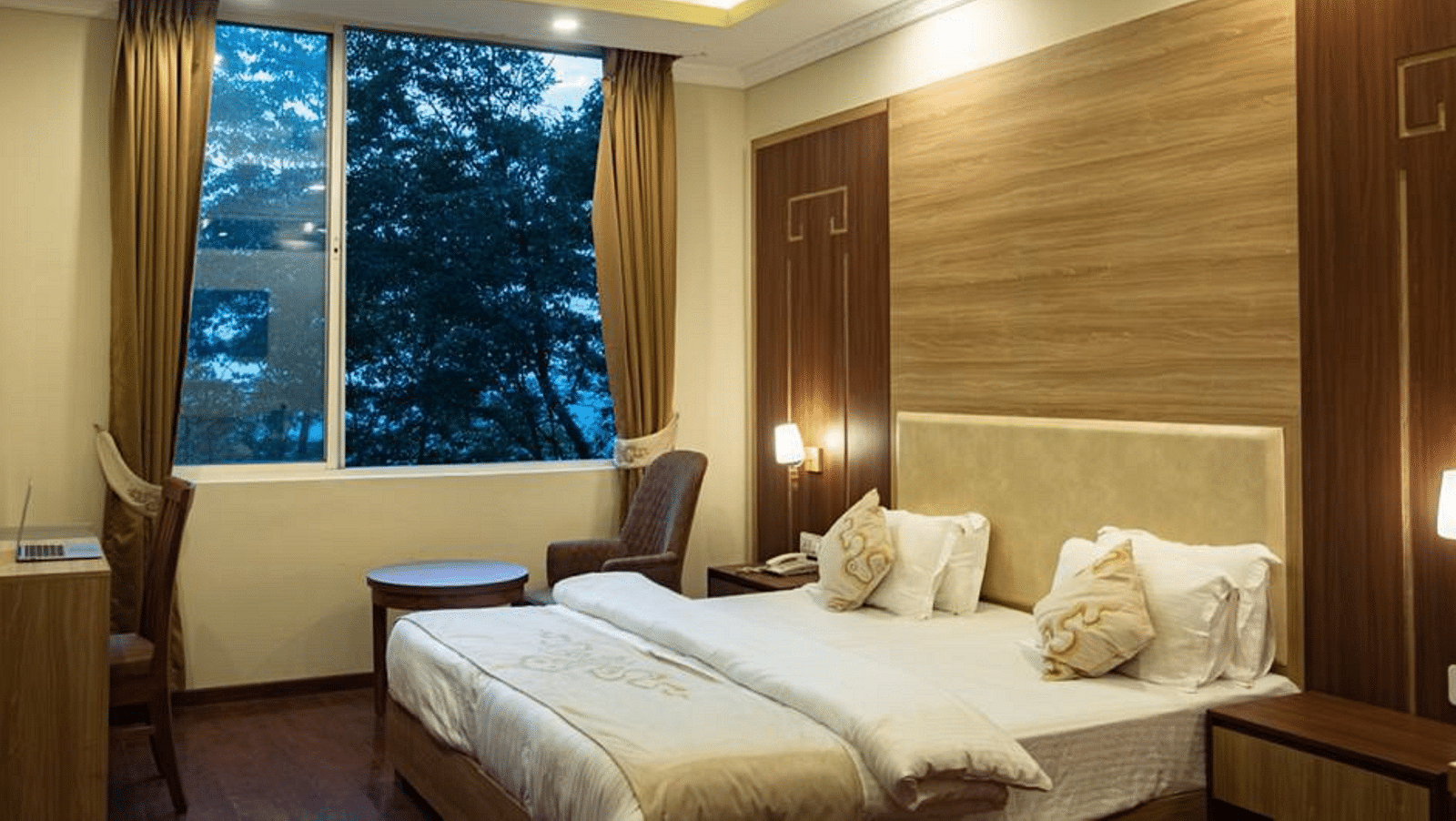 A queen bed with a large window next to it inside Deluxe Room at Sumitel Gangtok 
