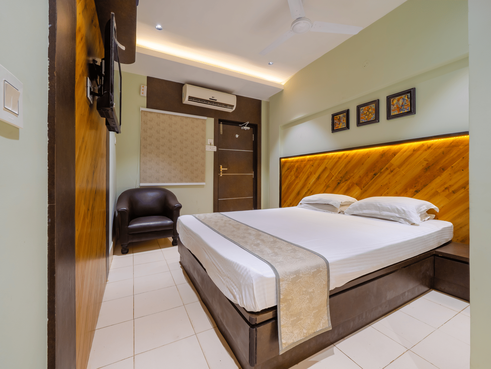 A minimalist hotel bedroom with a double bed, light-coloured walls, and a glimpse of the wooden entrance door - Hotel Dolphin Puri