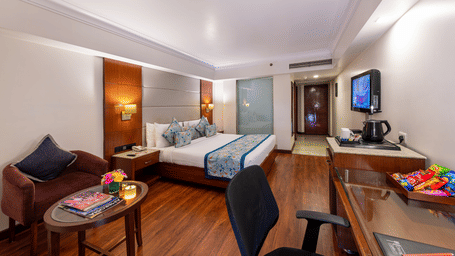 Cosy Club Room with double bed, study area, sofa, flat screen TV, and bright lighting at Lords Plaza Jaipur.