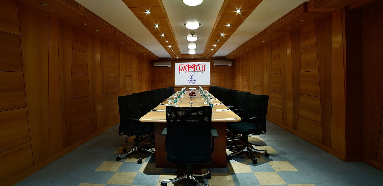 A modern boardroom with a long table, black chairs, and a projector screen at the end. - Tara, Comfort Hotel in Hyderabad - Ramoji Film City.