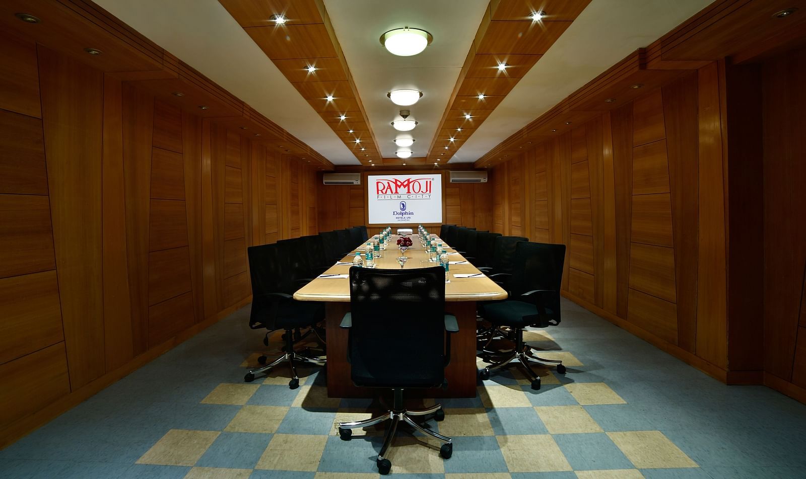 A modern boardroom with a long table, black chairs, and a projector screen at the end. - Tara, Comfort Hotel in Hyderabad - Ramoji Film City.
