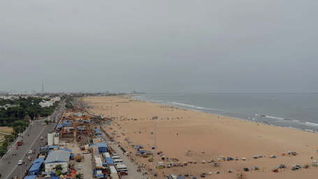 An aerial view of Marina Beach, the famous beach in Chennai, with waves crashing on the shores, cars on the road and sky in the background.
