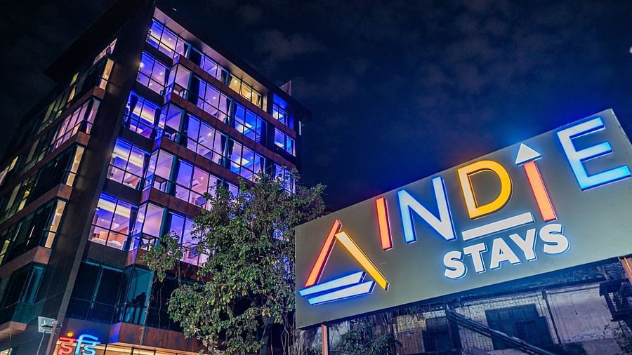 A night view of Indie Stays Mumbai International Airport, showcasing the illuminated name board on one side and the building's striking architecture on the other.