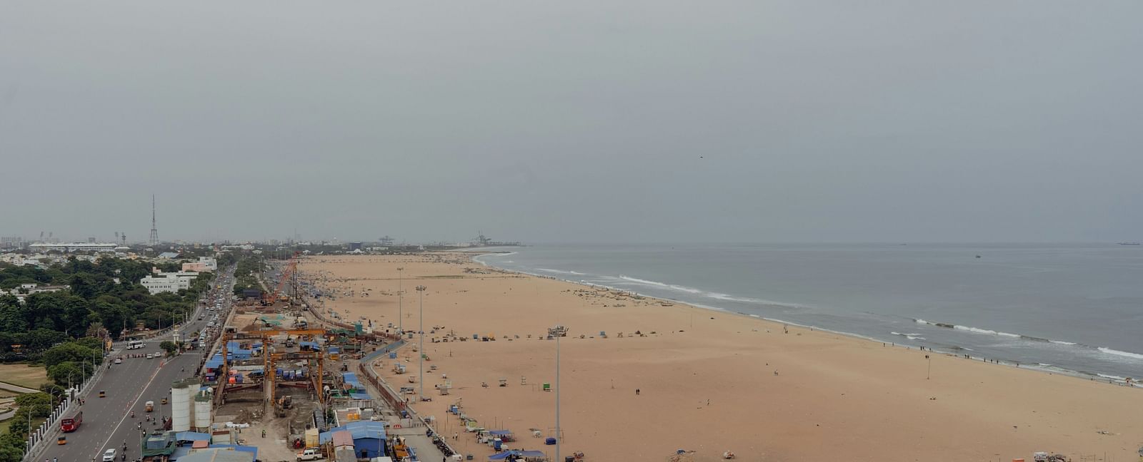 An overview of Marina Beach in Chennai with people, shops, road and vehicles in view.